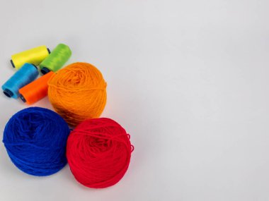 Kırmızı, mavi, sarı, yeşil ve turuncu da dahil olmak üzere çeşitli iplik makaraları ve topları içeren canlı bir kompozisyon. Renkli makaralar, daha büyük iplik toplarının yanına dizilmiştir, hepsi temiz beyaz arka plana karşıdır..