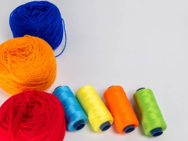 Kırmızı, mavi, sarı, yeşil ve turuncu da dahil olmak üzere çeşitli iplik makaraları ve topları içeren canlı bir kompozisyon. Renkli makaralar, daha büyük iplik toplarının yanına dizilmiştir, hepsi temiz beyaz arka plana karşıdır..