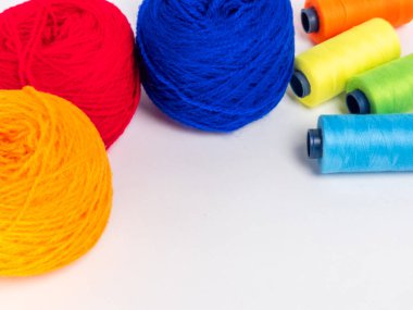 Kırmızı, mavi, sarı, yeşil ve turuncu da dahil olmak üzere çeşitli iplik makaraları ve topları içeren canlı bir kompozisyon. Renkli makaralar, daha büyük iplik toplarının yanına dizilmiştir, hepsi temiz beyaz arka plana karşıdır..