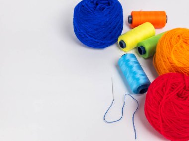 Bu resim beyaz bir yüzeye dizilmiş renkli iplik topları ve iplik makaralarının bir derlemesini içerir. Mavi ipliğin yanına bir iğne yerleştiriliyor. Kompozisyon basit, iplik ve ipliğin canlı renkleri ve dokularına odaklanarak..