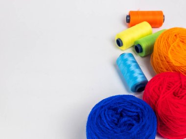 Kırmızı, mavi, sarı, yeşil ve turuncu da dahil olmak üzere çeşitli iplik makaraları ve topları içeren canlı bir kompozisyon. Renkli makaralar, daha büyük iplik toplarının yanına dizilmiştir, hepsi temiz beyaz arka plana karşıdır..