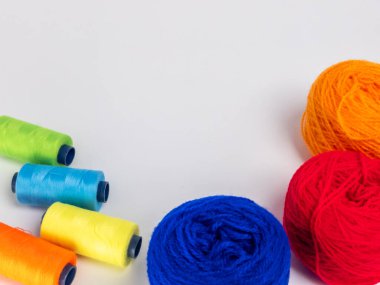 Kırmızı, mavi, sarı, yeşil ve turuncu da dahil olmak üzere çeşitli iplik makaraları ve topları içeren canlı bir kompozisyon. Renkli makaralar, daha büyük iplik toplarının yanına dizilmiştir, hepsi temiz beyaz arka plana karşıdır..