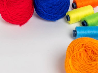 Kırmızı, mavi, sarı, yeşil ve turuncu da dahil olmak üzere çeşitli iplik makaraları ve topları içeren canlı bir kompozisyon. Renkli makaralar, daha büyük iplik toplarının yanına dizilmiştir, hepsi temiz beyaz arka plana karşıdır..