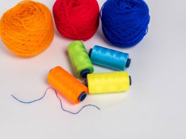 Bu resim beyaz bir yüzeye dizilmiş renkli iplik topları ve iplik makaralarının bir derlemesini içerir. Mavi ipliğin yanına bir iğne yerleştiriliyor. Kompozisyon basit, iplik ve ipliğin canlı renkleri ve dokularına odaklanarak..