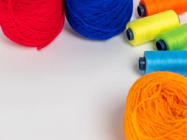 Kırmızı, mavi, sarı, yeşil ve turuncu da dahil olmak üzere çeşitli iplik makaraları ve topları içeren canlı bir kompozisyon. Renkli makaralar, daha büyük iplik toplarının yanına dizilmiştir, hepsi temiz beyaz arka plana karşıdır..