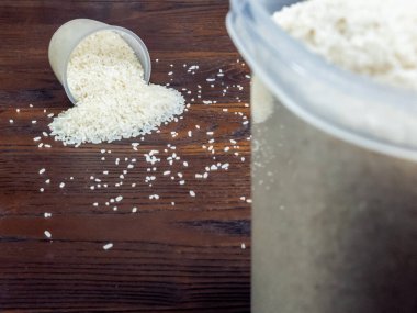 Beyaz pirinç tanelerinin bir ölçü kabından koyu kahverengi ahşap bir yüzeye döküldüğü yakın çekim..