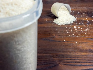 Bir görüntüde ölçü kabından dökülen pirinçle ahşap bir masa sergileniyor. Sol tarafta büyük bir kap pirinç görülebilir. Sahne, günlük hayatın, mutfak hazırlığının ve yemeğin anlamını taşıyor..