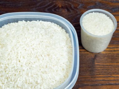 Plastik bir kapta pişmemiş pirinç ve ölçü kabının yakın plan çekimi. Pirinç beyazdır ve kabı doldurur..