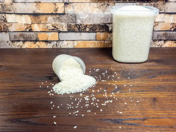 Yakından çekilen bir fotoğrafta bir ölçü kabı ahşap bir masanın üzerine devrilmiş ve pirinçler etrafa saçılmış. Pirinç dolu büyük bir konteynır yakınlarda dikiliyor. Sahne tuğla bir duvara dayanıyor, basit bir mutfak ya da kiler ayarlanıyor..