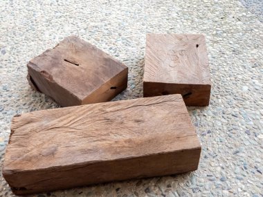 Üç dikdörtgen tahta blok benekli çakıl benzeri bir yüzey üzerinde sergileniyor. Tahtanın doğal, yıpranmış bir görünüşü var. Görünür tahıl ve kusurları var. Yaşını ve kullanım alışkanlığını gösteriyor..