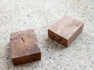 Yakın plan çekimde iki dikdörtgen tahta blok benekli ve desenli bir yüzey üzerinde duruyor. Bloklar doğal ve yıpranmış bir görünüm sergiliyor. Görünür ahşap tanecikleri ve kusurlarıyla..