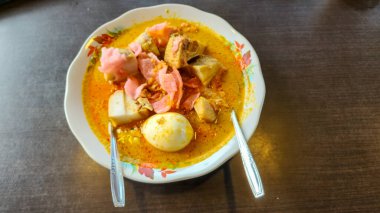 Bu resimde Endonezya Lontong Sayur tabağı yer almaktadır. Çanak yakın plan çekimde sunuluyor, içeriğinin canlı renkleri ve dokuları sergileniyor..