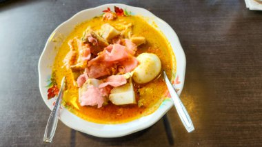 Yakın plan çekimde Endonezya 'dan canlı bir Lontong Sayur yemeği, popüler bir Güneydoğu Asya yemeği sergileniyor. Buharda pirinç kekleri (lontong) zengin, hindistan cevizi sütü bazlı sebze yahnisi, tofu, haşlanmış yumurta ve pembe krakerler yer alıyor..