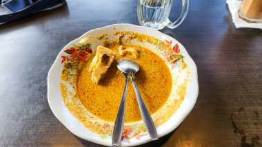 Güneydoğu Asya yemeği içeren bir tabağın yukarıdan aşağıya bakışı. Tabakta canlı, turuncu köri sosuna batırılmış tofu parçaları yer alıyor. Tabakta iki kaşık dinleniyor. Bir bardak su ve bir bardak görünür.