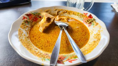 Bir tabak Endonezya körisinin yakın çekimi, muhtemelen rendang ya da benzer bir yemek, portakal-kahverengi soslu. Tabak, çiçek desenli beyaz bir tabakta servis ediliyor.. 