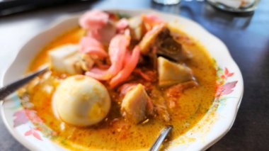 Bu yakın plan çekimde bir tabak pirinç keki, sebze, yumurta ve kraker ile popüler bir yemek olan Endonezya Lontong Sayur yer alıyor. Tabak zengin, lezzetli bir köri sosuyla yıkanır ve görsel olarak çekici ve iştah açıcı bir görüntü yaratır..