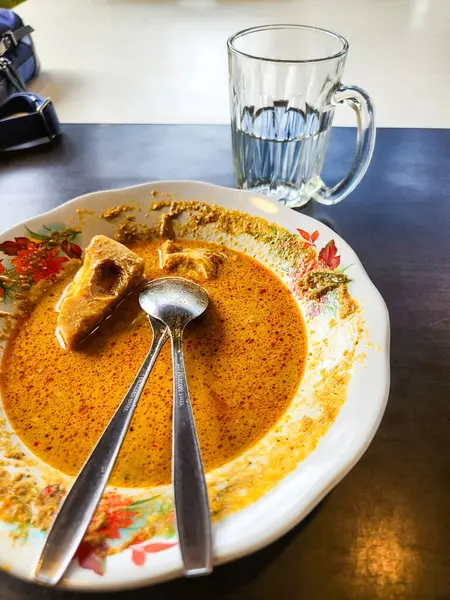 İki kaşıkla servis edilen tofu ya da benzer bir malzemeyle servis edilmiş bir tabak köri ile yakın çekim. Bir bardak su tabağın yanında oturur. Yemek sarı bir sosta, tabağın etrafında da bazı kalıntılar var..