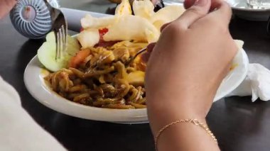 Endonezya eriştesinin çeşitli malzemeleriyle lezzetli bir tabağın tadını çıkaran kişi.