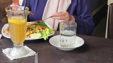 Bir kadın açık hava restoranında yemek yiyip içki içiyor.