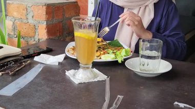 Bir kadın, açık hava kafesinde serinletici bir içecekle yemekten zevk alıyor.