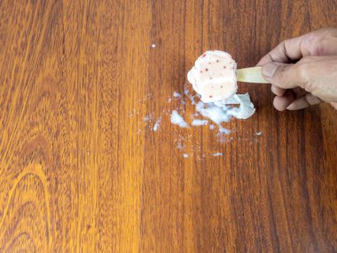 Ahşap bir yüzey üzerinde kısmen erimiş dondurmayı tutan bir elin yakın çekimi. Dondurma döküldü, ortalık kan gölüne döndü. Görüntü yazın bir anını yakalar, odunun dokusuna ve erime ikramına odaklanır..