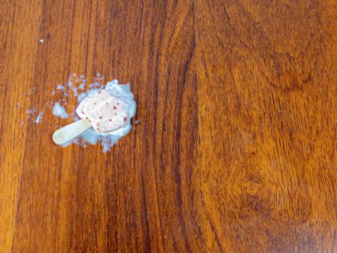 Yakın çekim, erimiş dondurmayı ahşap bir yüzeyde yatarken yakalar. Görüntü, ahşabın dokusunu, eriyen dondurmayı ve tahta çubuğu sergiliyor..