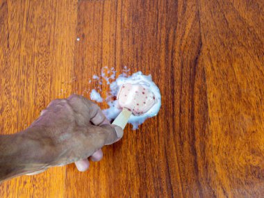 Tepeden çekilen bir resimde, bir elin, kısmen erimiş buzlu çubuğu ahşap bir yüzeyde tuttuğu görülüyor. Buzlu dondurma erimeye ve yayılmaya başladı. Dondurma ve meyve suları odunların üzerinde bir havuz oluşturuyor..