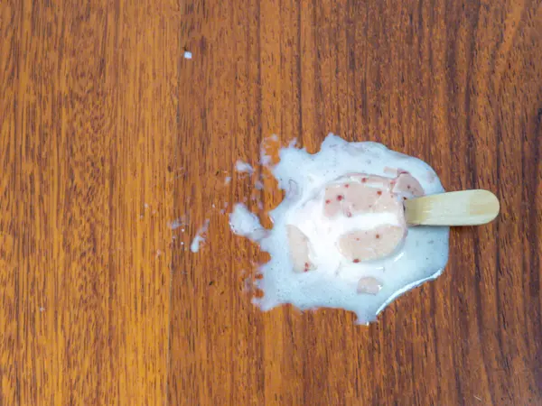 Ahşap zeminde erimiş dondurmanın yukarıdan aşağı görüntüsü. Dondurma kısmen bozulmamış, görünen kırmızı benekler ve tahta bir sopayla.. 