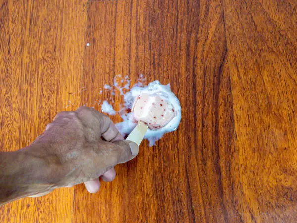 Tepeden çekilen bir resimde, bir elin, kısmen erimiş buzlu çubuğu ahşap bir yüzeyde tuttuğu görülüyor. Buzlu dondurma erimeye ve yayılmaya başladı. Dondurma ve meyve suları odunların üzerinde bir havuz oluşturuyor..