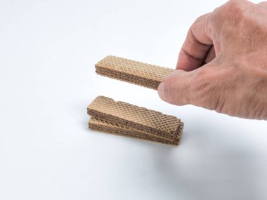 Beyaz bir yüzey üzerinde çikolatalı gofret kurabiyesi tutan bir elin yakın çekim çekimi. Görüntü, kurabiyelerin ve elin dokusunu ve detaylarını vurgular. Kompozisyon basit, konuya odaklanmış..