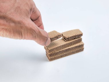 Yakın plan çekimde beyaz arka planda çikolatalı gofret kurabiyelerini düzenleyen bir el görülüyor. Görüntü gofretlerin dokusunu ve çikolata dolgusunu vurguluyor. Kompozisyonda inşaat ya da inşaat kavramı vurgulanıyor.