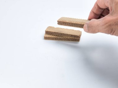 Beyaz arka planda bir yığın başka kurabiyeyle birlikte çikolatalı kurabiye tutan birinin yakın plan fotoğrafı. Resim, katmanların altını çizerek, gofretlerin dokusunu ve detaylarını yakalar. Arka plan temiz ve parlak..