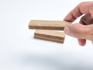 Bir el çikolatalı gofret kurabiyesini beyaz arka plandaki benzer kurabiyelerin üzerinde tutuyor. Görüntü, gofretlerin dokusuna ve detaylarına ve çikolata dolgusuna odaklanıyor..