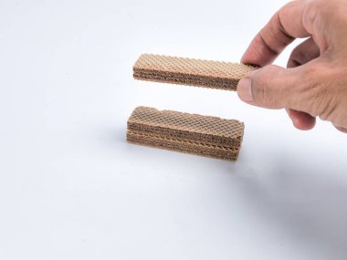 Benzer kurabiyelerin üzerinde çikolatalı kurabiye tutan bir elin olduğu yakın çekim bir stüdyo resmi. Görüntü temiz beyaz bir arkaplana göre ayarlanır, atıştırmalığın dokusunu ve detaylarını vurgular.