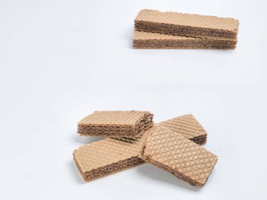 Yakın plan çekimde el değmemiş beyaz bir arkaplana yerleştirilmiş birkaç çikolatalı gofret kurabiyesi yer alıyor. Gofretler dikdörtgen, açık kahverengi waffle desenli ve koyu çikolata dolgulu..