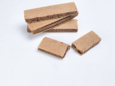 Yakın plan çekimde çikolatalı gofretlerden oluşan bir koleksiyon sergileniyor, bazıları istiflenmiş ve diğerleri parlak beyaz bir yüzeye saçılmış. Gofretlerin parlak, dokulu bir görünüşü var. Görünür katmanları ve zengin bir çikolata dolgusu var..