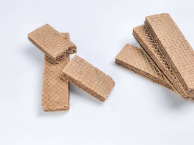 Beyaz bir yüzeye saçılmış çikolatalı gofret kurabiyelerinin yakın plan bir çekimi. Kurabiyeler dikdörtgen ve katmanlı, dışı çıtır çıtır ekmek ve çikolata kremalı. Bazı gofretler bütken, diğerleri kırık..