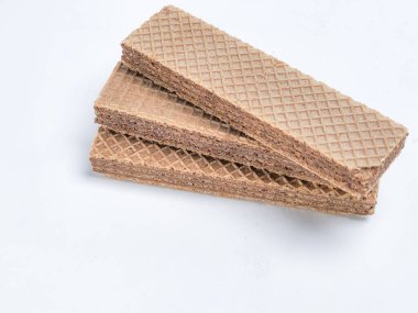 Yakın plan çekimde, temiz beyaz bir yüzey üzerinde üç adet dikdörtgen çikolatalı gofret sergilenir. Gofretlerin belirgin bir waffle deseni ve çikolata dolgulu zengin, kahverengi bir rengi var. Görüntü iyi aydınlatılmış, dokuları ve detayları vurguluyor.. 