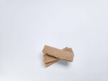 Beyaz arka planda bir yığın çikolatalı gofret kurabiyesi. Kurabiyeler, gözleme desenli dikdörtgen şeklinde ve zengin kahverengi renkteler. Beyaz arkaplan, kurabiyeleri vurgulayarak temiz bir kontrast sağlıyor.