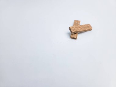 İki çıtır çikolatalı gofret kurabiyesinin yakın plan görüntüsü. Çapraz şeklinde dizilmiş, düz beyaz arka planda. Görüntü, kendi katmanlarını gösteren gofretlerin dokusunu ve detaylarını vurgular. Kompozisyon basit ve temiz..