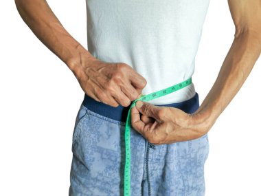 Yeşil bir mezura ile belini ölçen bir adamın yakın plan çekimi. Adam beyaz bir tişört ve mavi bir şort giyiyor. Bu görüntü kilo kaybı, sağlık, sağlık, vücut ölçümleri ve makaleler için mükemmel yaşam tarzı seçimlerini temsil edebilir..