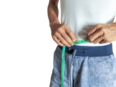 Yeşil bir mezura ile belini ölçen bir adamın yakın çekimi. Beyaz tişört ve mavi şort giyiyor. Adam kilosunu ya da formda olup olmadığını kontrol ediyor. Görüntü iyi aydınlatılmış, iyi detaylarla. Bele odaklan..