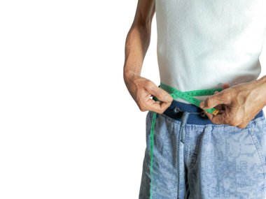 Beyaz atlet ve mavi şort giyen yaşlı bir adam, yeşil bir mezura ile belini ölçer. Görüntü kilo verme ve sağlıklı yaşama odaklanıyor. Adamın ellerini ve bel bölgesini beyaz bir arka plana vurguluyor..