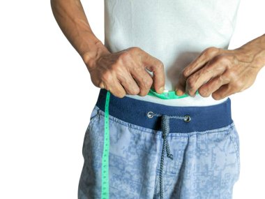 Yakın çekim, yeşil bir mezura kullanarak belini ölçen bir adamı yakalar. Bandı karnına saran adamın ellerine odaklanarak ağırlık yönetimi ve sağlık değerlendirmesi kavramını vurguluyor..