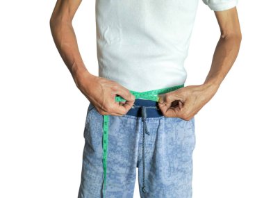 Beyaz tişörtlü ve mavi şortlu bir adam yeşil bant ölçüsüyle belini ölçer. Görüntü bel, eller ve ölçüm sürecine odaklanıyor. Yakın çekim, vücudun detaylarını ve ölçüm bandını vurguluyor..