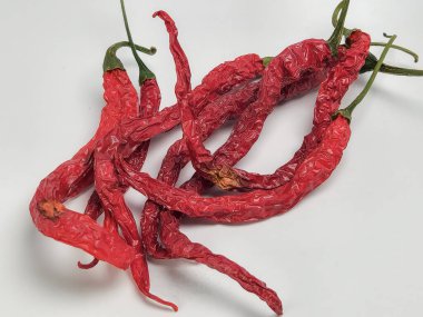 Sade beyaz bir arka planda birkaç kurutulmuş kırmızı biberli yakın çekim. Biberler buruşuk bir doku ve değişik şekiller sergiler. Görüntü, kırmızı zengin rengi ve kuru kırmızı biberlerin karmaşık detaylarını vurguluyor..