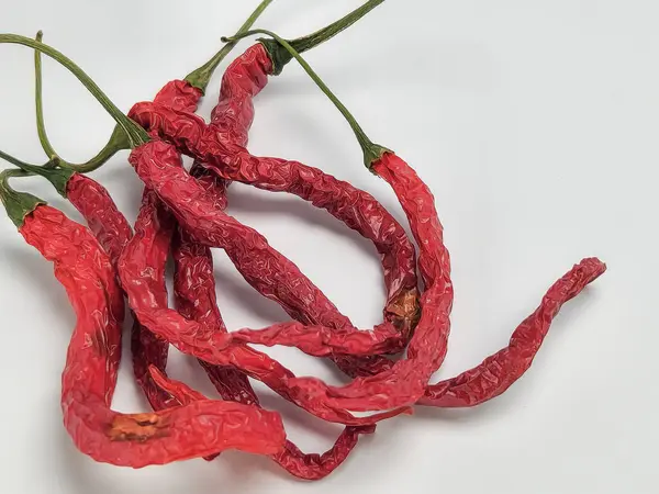 Birkaç kurutulmuş kırmızı biberli yakın çekim stüdyo fotoğrafı. Biberler bir yığın halinde dizilir ve kurumuş dokularını göstermek için buruşuk ve buruşuk olurlar. Arka plan temiz, parlak beyaz, kırmızı biberleri öne çıkarıyor..