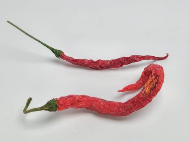 Bu resim, beyaz arka planda izole edilmiş iki kurutulmuş kırmızı biber içeriyor. Biberler buruşur ve kurumuş görünürler, dokuları ve renkleri ortaya çıkar. Kompozisyon basit, doğal forma ve canlı kırmızı renge odaklı. 
