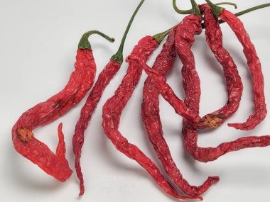 Beyaz arka planda birkaç kurutulmuş kırmızı biberin yakın plan çekimi. Biberler buruşuk ve buruşuk, kurumuş dokularını ve renklerini gösteriyor. Çekim iyi aydınlatılmış, dokuları vurguluyor..