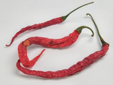 Yakın çekim bir stüdyo çekiminde düz beyaz arka planda üç kurutulmuş kırmızı biber yer alır. Biberler buruşmuş ve uzamış, yeşil sapları var. Biberlerin dokusunu ve rengini vurguluyor. Kurumuş ve yaşlanmış hallerini gösteriyor.